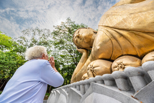Elderly Thai woman praying to giant reclining Buddha statue at temple