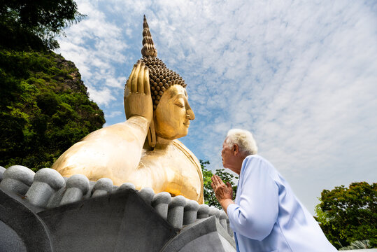 Elderly Thai woman praying to giant reclining Buddha statue at temple