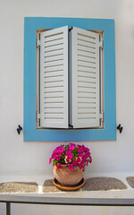 window surrounded in blue  with closed shutters of a house with white facade in Greece