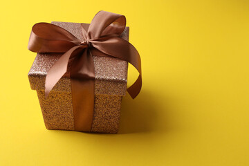 Gift box with a bow on a yellow background, top view. Space for text
