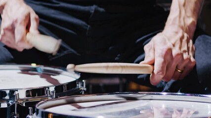 Close-up of a drummer's hands playing a snare drum with wooden sticks.