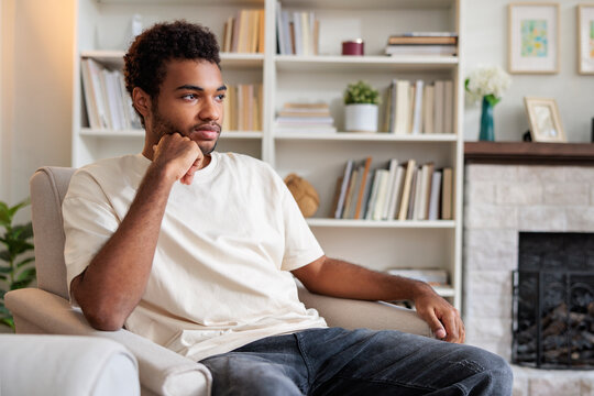 Thoughtful young man sitting with hand on chin at home