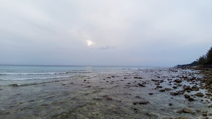 Tranquil coastal view with sunset peeking through cloudy sky.