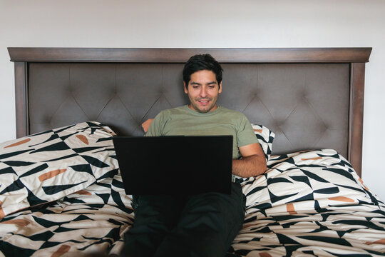 Latin man working from home using laptop in bed