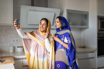 Arab women taking a selfie together in the kitchen.