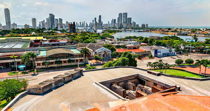 View of modern high-rises and waterfront neighborhoods in Cartagena, Colombia seen from the elevated platform of Castillo San Felipe de Barajas. The photo contrasts colonial stone structures in the