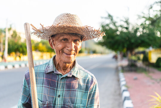 Elderly street sweeper smiling at camera in city of Thailand