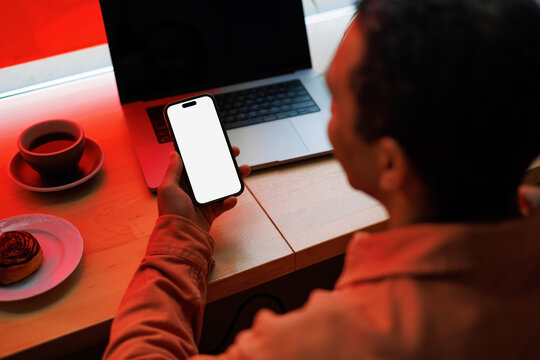 Man Holding Smartphone with Blank White Screen at Coffee Table 