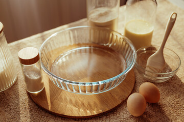 A clear glass flan dish sits on a wooden board, surrounded by baking ingredients.