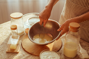 A person wearing a striped apron whisks ingredients in a metal bowl, surrounded by other baking...