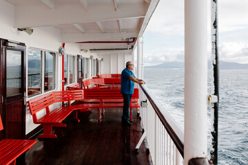 Elderly man resting on the railing of a ship gazing at the sea
