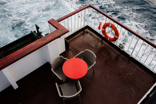 A table with chairs around it at the back of a moving ship
