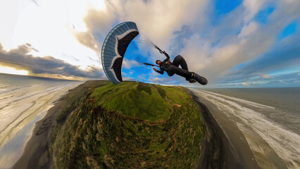 Extreme paragliding pilot soaring in the New Zealand beach at sunset. Adventure concept