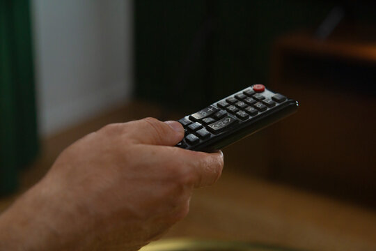 Hand holding remote control, changing channels on television
