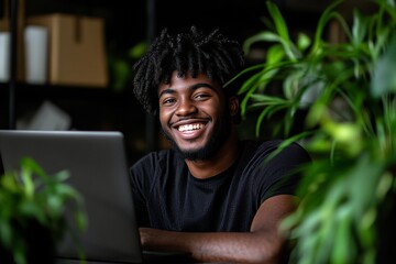 Young man smiling while working on laptop surrounded by indoor plants in a cozy home office setting