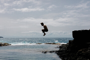 Long shot of a person diving into a natural basin among sharp rocks