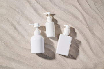 Three white cosmetic bottles on textured beige sand