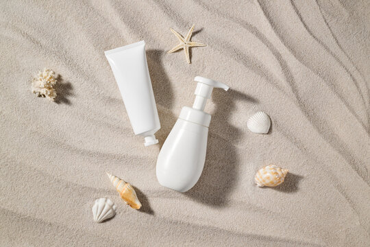 White cosmetic products and seashells arranged on beach sand