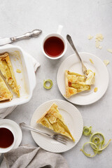 A slices of rhubarb pie or tart on a white plates with cups of tea. summer breakfast concept .Tart with sour cream filling . Healthy homemade summer dessert, Top view, copy space.