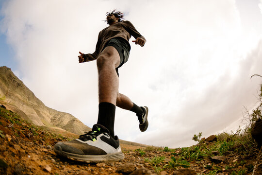 Low-angle shot of a professional runner jogging along a rocky trail