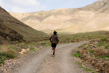 Back view of a man in athletic wear running across a dirt trail