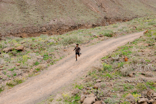 A lone runner on a curved dirt road, with dry shrubs