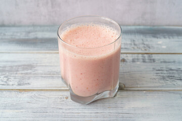 Fresh pink smoothie in clear glass on light gray wood background. Healthy refreshing drink for wellness and nutrition concept. Natural and organic beverage.