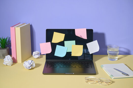 A laptop surrounded by sticky notes, a notepad, and other elements