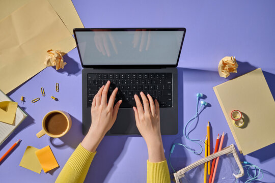Topview of a person typing on a laptop, surrounded by workspace