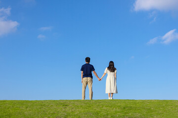 A young couple holding hands, seen from behind on the grass