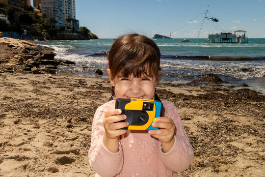 Little girl taking pictures with disposable camera at Benidorm beach
