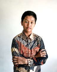 A teenage boy wearing a batik shirt posing confidently with arms crossed and a slight smile, isolated on white