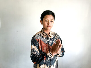 A teenage boy wearing a batik shirt doing a respectful greeting with hands together, isolated on white