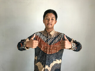 A teenage boy wearing a batik shirt is giving two thumbs up, isolated on white