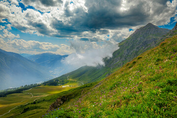 Green slopes and surrounding mountains under beautiful dramatic sky near Colle delle Finestre in Piedmont, Italy.