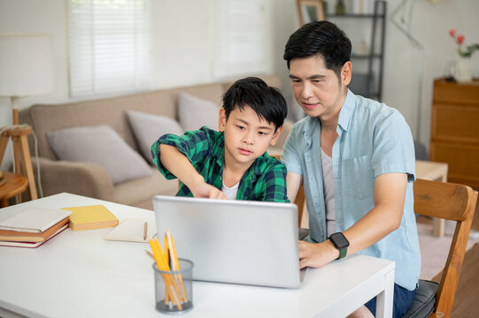 A son pointing at laptop screen while asking his father about homework in their house.
