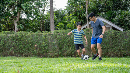 Fototapeta premium Father and son having fun playing soccer or football in their home's backyard or green grass field.