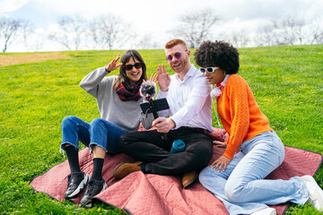 Three content creators waving at the camera while recording a video blog outdoors using a...
