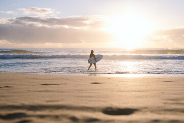 Surfer walking into ocean at sunrise on sandy manly beach