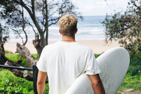 Surfer watching the ocean waves holding surfboard on the beach