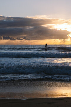 Surfer waiting for the perfect wave at sunrise under cloudy sky