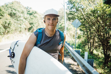 Surfer walking along the road carrying surfboard on sunny day