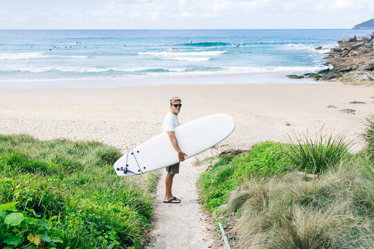 Surfer walking up a sandy path from the beach carrying his surfboard