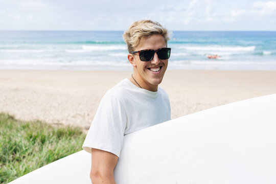 Young surfer smiling and holding his surfboard on the beach
