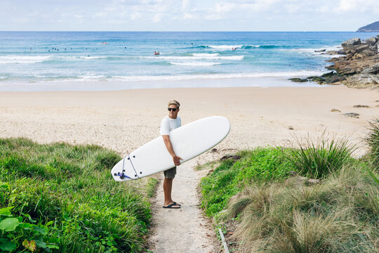 Surfer walking from beach towards ocean with surfboard under arm