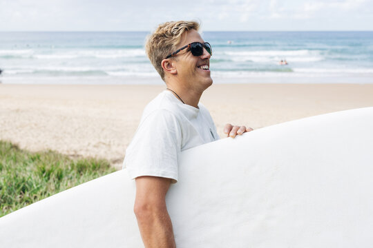 Happy surfer holding surfboard on beach, enjoying summer lifestyle