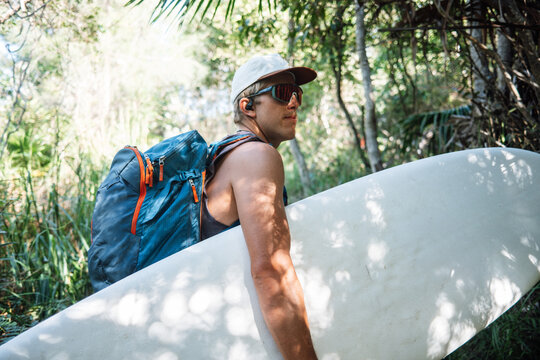 Surfer walking through tropical forest carrying surfboard and backpack