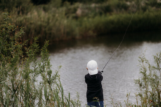 Child casting fishing rod in pond surrounded by natural greenery