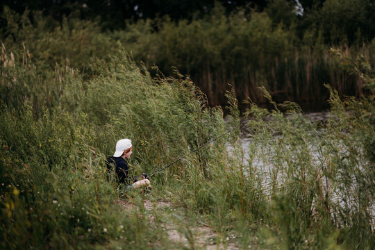Young boy quietly fishing alone by overgrown riverbank reeds