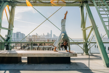 Woman performs handstand on bench with NYC skyline behind her